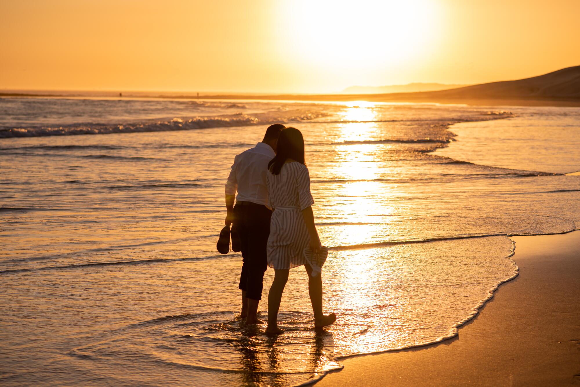 Couple walking along coastline during sunset